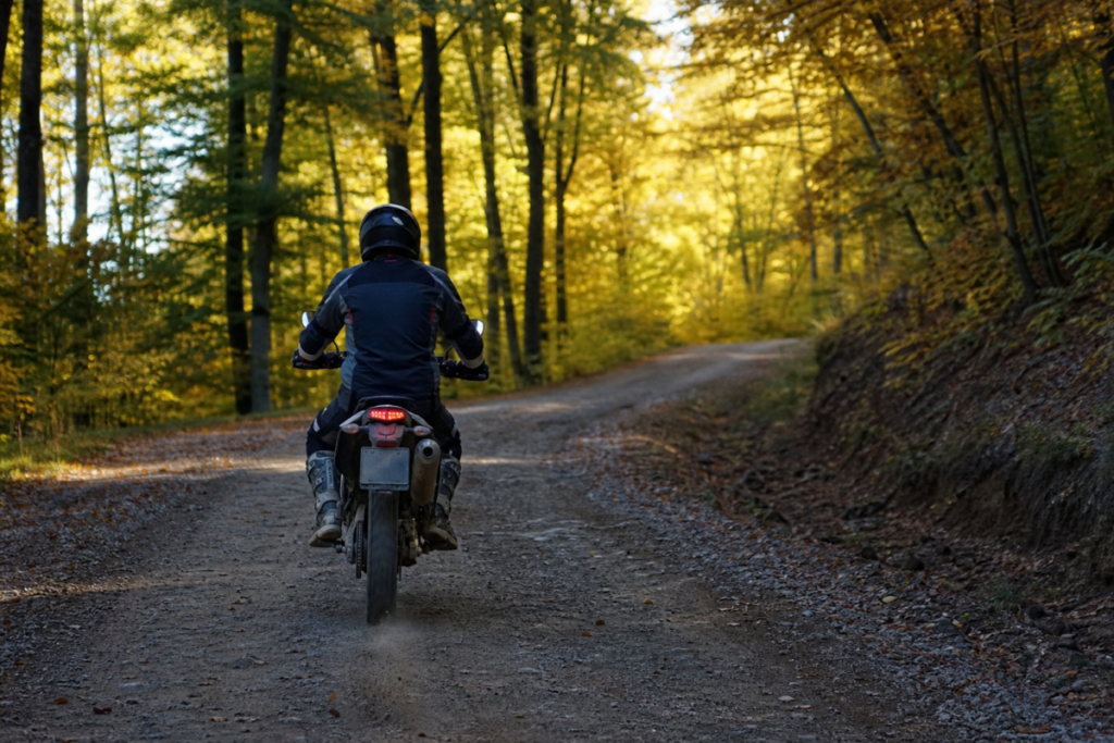 Moto d'enduro homologuée sur un chemin forestier ouvert à la circulation, pilote vu de dos en tenue d'enduro